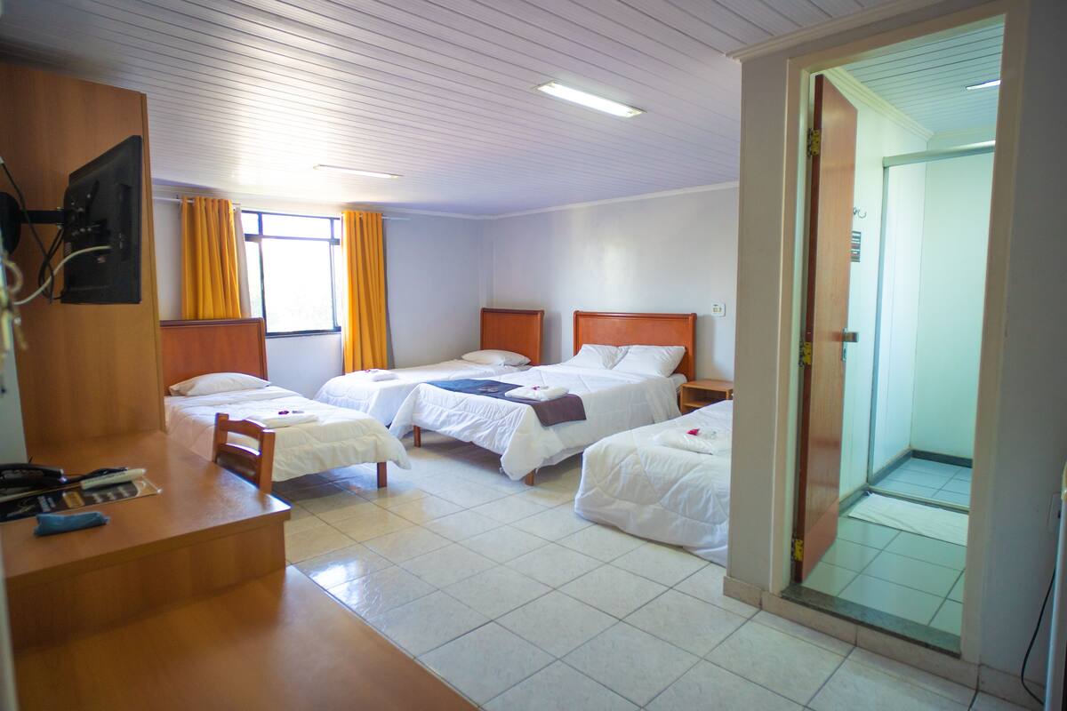 Una habitación de hotel con tres camas individuales, un escritorio y un espacio con ducha.