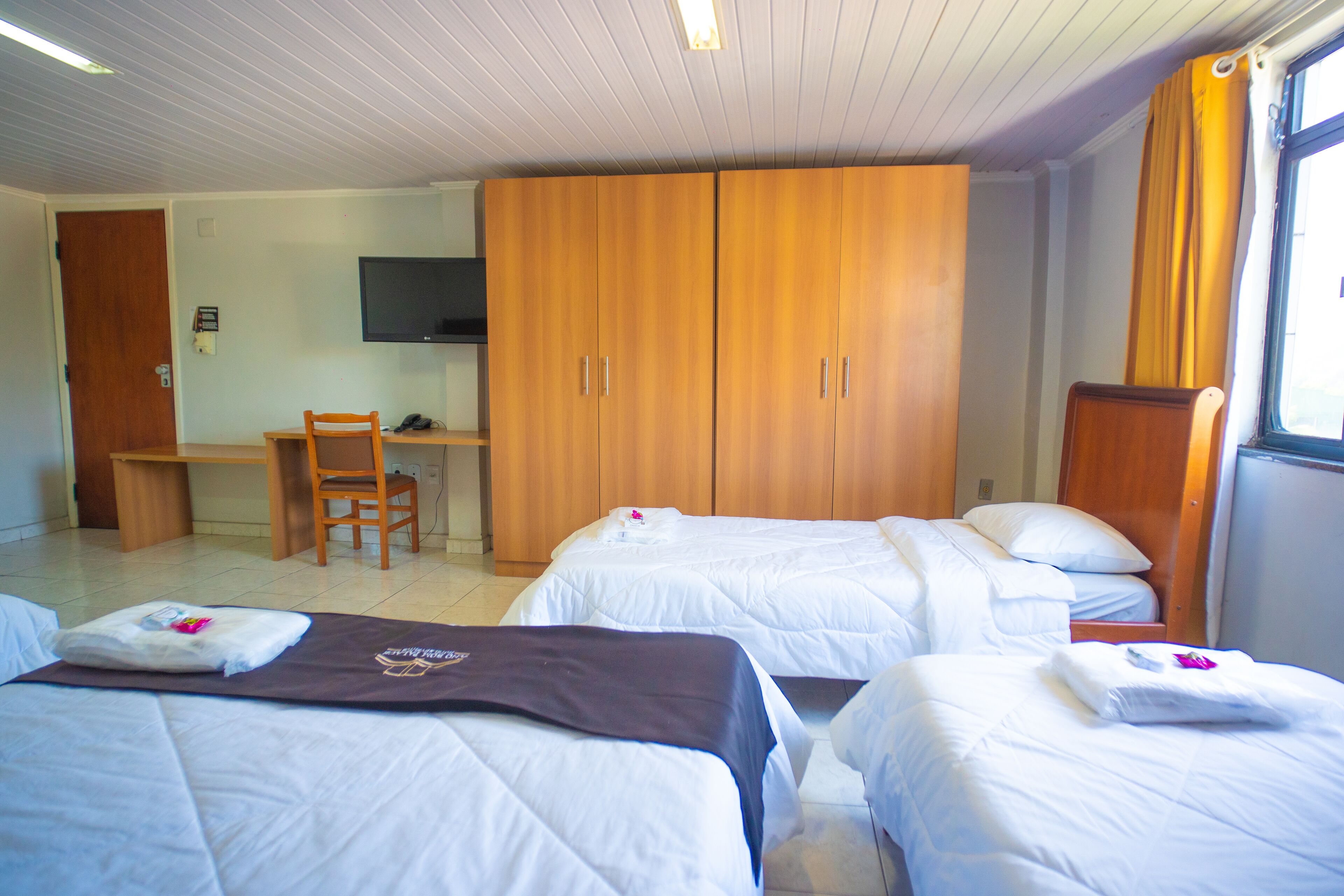 Quarto de hotel com duas camas, uma escrivaninha, uma cadeira e uma televisão.