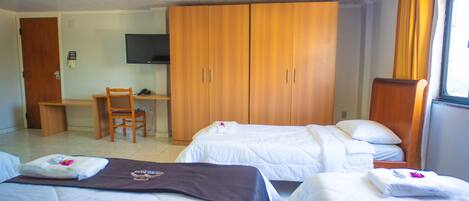 A hotel room with two beds, a desk, a chair, and a TV.