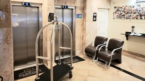 Un vestíbulo de hotel con dos ascensores, una recepción y un área de espera con sillas.