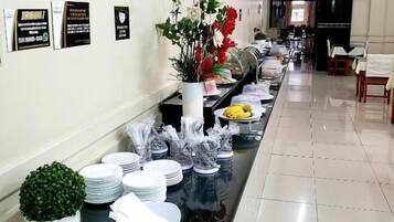 A hotel corridor with a buffet setup, including plates, bowls, and a potted plant.