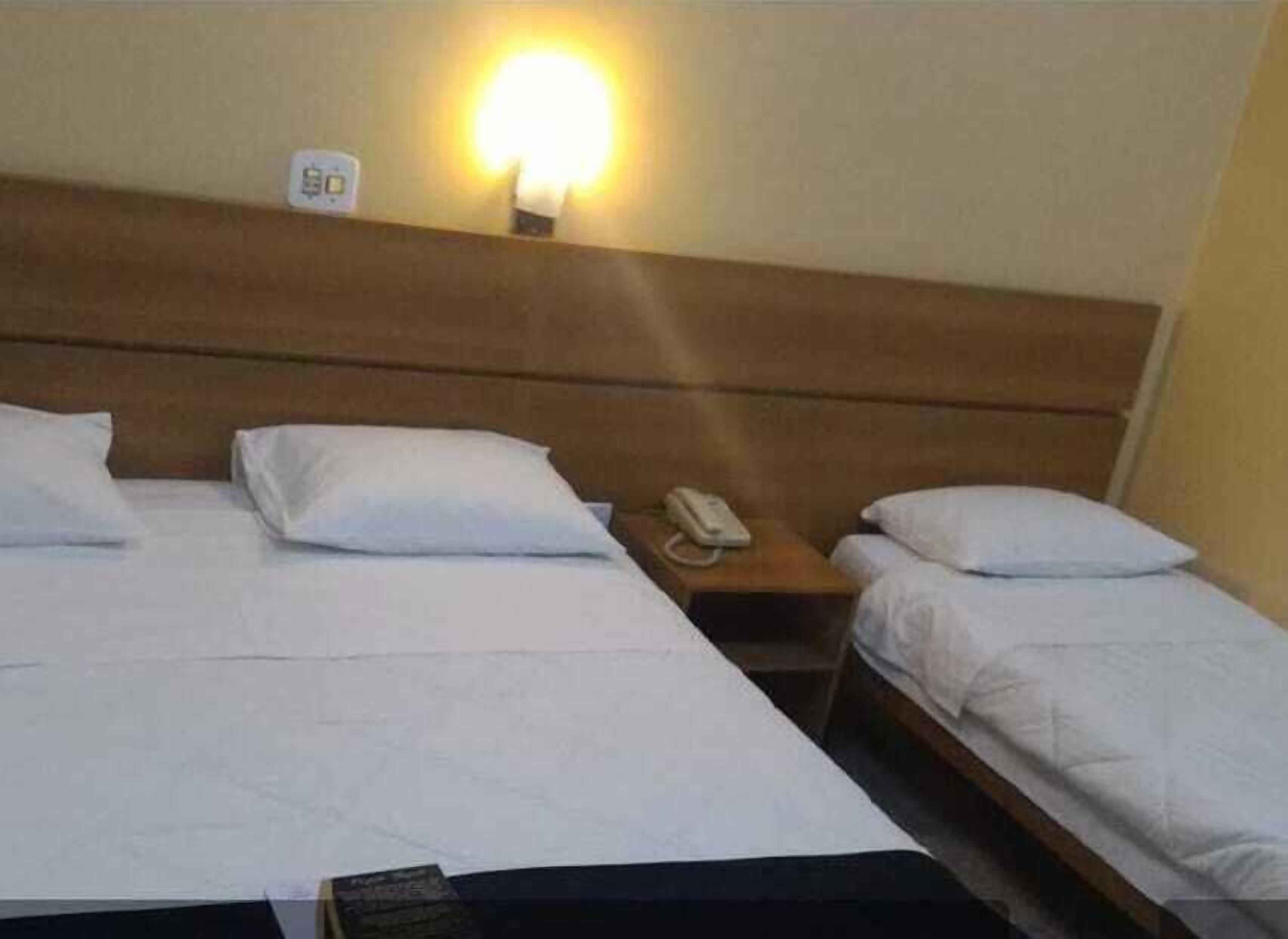 Une chambre d’hôtel avec deux lits, une table de chevet avec un téléphone et une lampe fixée au mur.