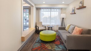 A hotel room with a sofa, ottoman, chair, and a small table.