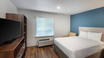 Een hotelkamer met een bed, een televisie, een raam met jaloezieën en een wandheater.
