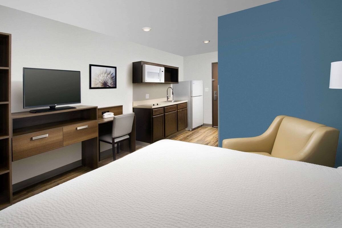 Una moderna camera d'albergo con un letto, una scrivania con TV a schermo piatto, una sedia, angolo cottura e una parete di colore blu.