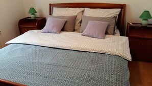 A neatly made bed with a patterned bedspread and pillows, two bedside tables with lamps, and a wooden headboard. - Beautiful apartment in center Sarajevo (Sarajevo)
