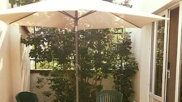 A patio with a round table and chairs, a large umbrella, and a tiled floor.