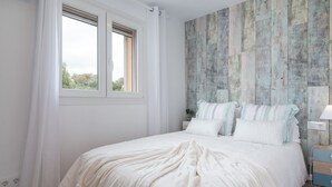 A bedroom with a large bed, a window with curtains, a nightstand with a lamp, and a wooden wall panel.