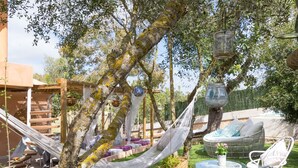 A hammock hanging from a tree, surrounded by outdoor furniture, including a wicker chair and a small round table with a potted plant.