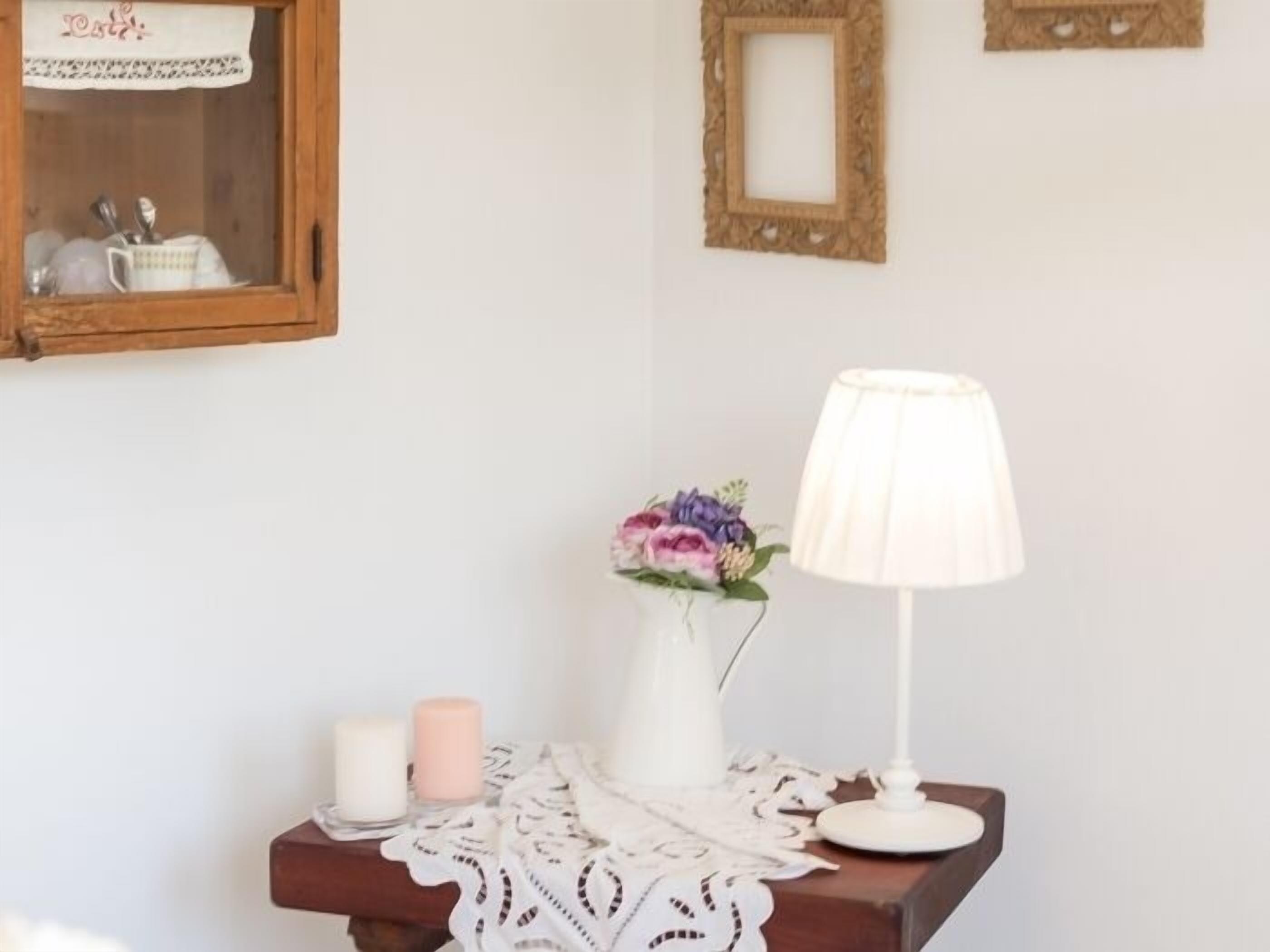 A small table with a white vase of flowers, a white candle, and a white lamp.