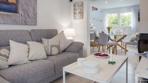 A modern living room with a grey sofa, patterned cushions, a white coffee table, and a dining area with a glass table and chairs.