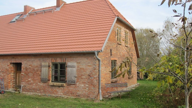 A brick house with a red tiled roof, a wooden door, and a bench outside.
