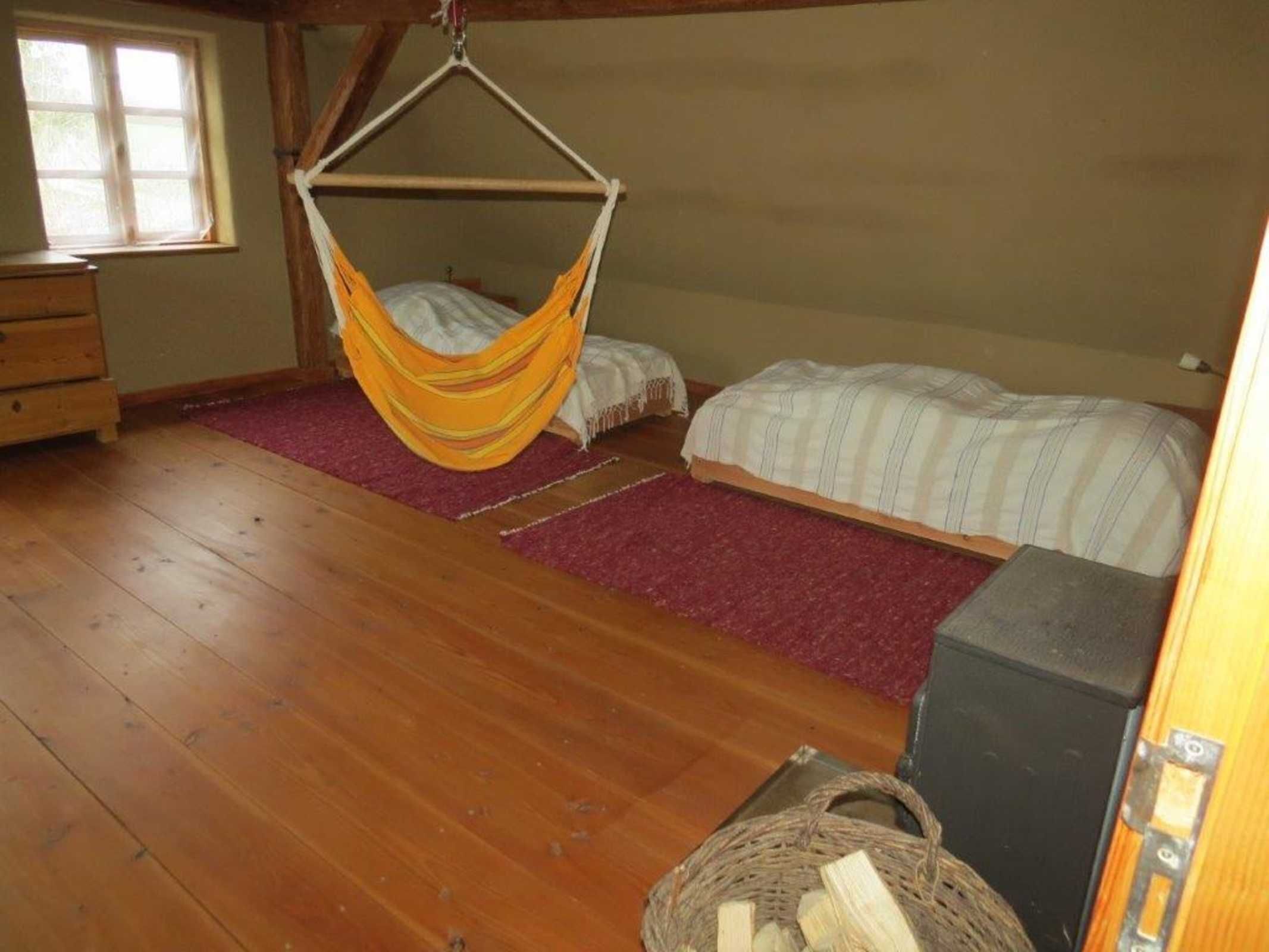Une pièce avec un plancher en bois, un lit-hamac, un lit classique, une commode et une fenêtre.