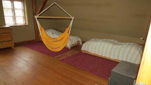 A room with a wooden floor, a hammock bed, a standard bed, a dresser, and a window.