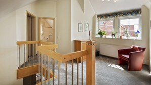 Un intérieur moderne avec un escalier en bois, un fauteuil rouge et une fenêtre agrémentée de plantes en pot.