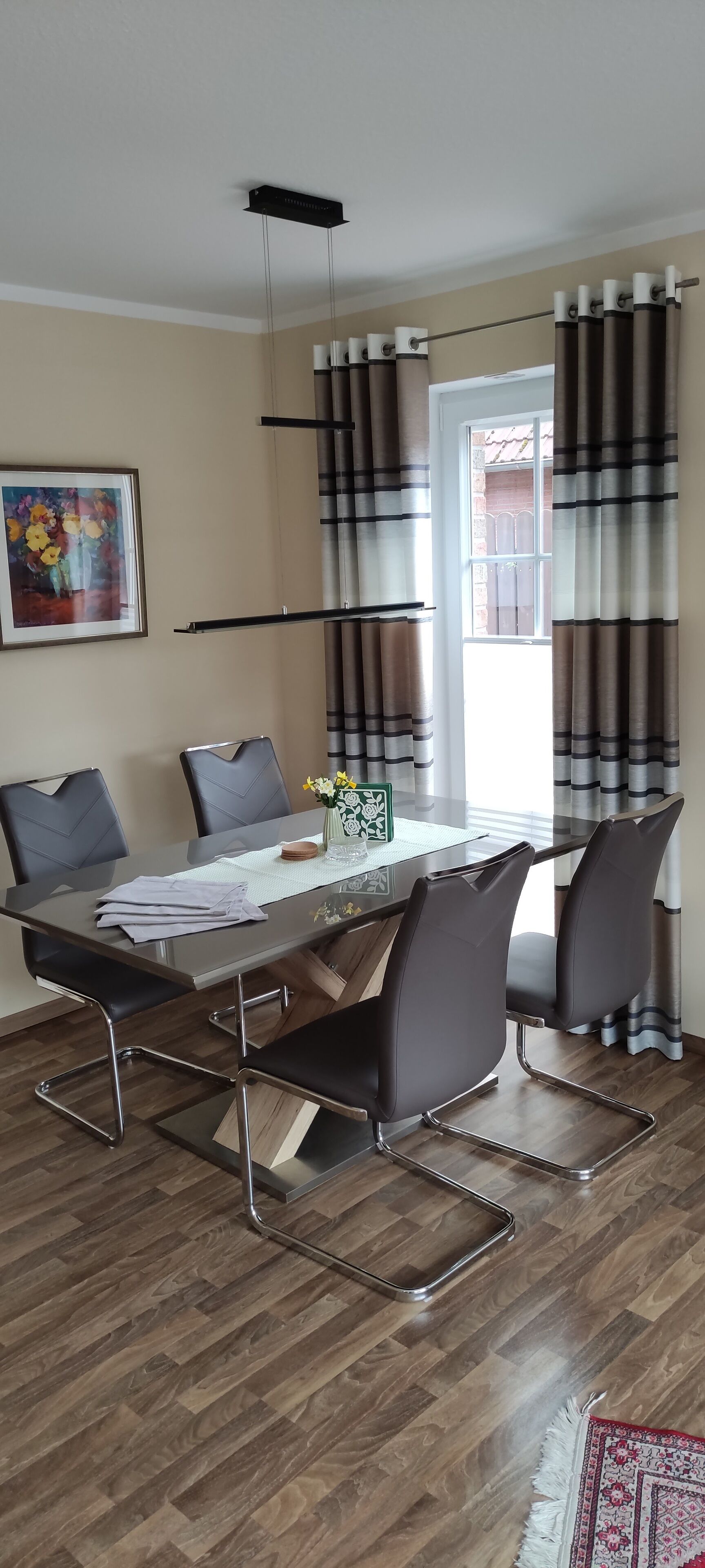 A dining area with a glass table, metal chairs, a vase with flowers, and striped curtains.