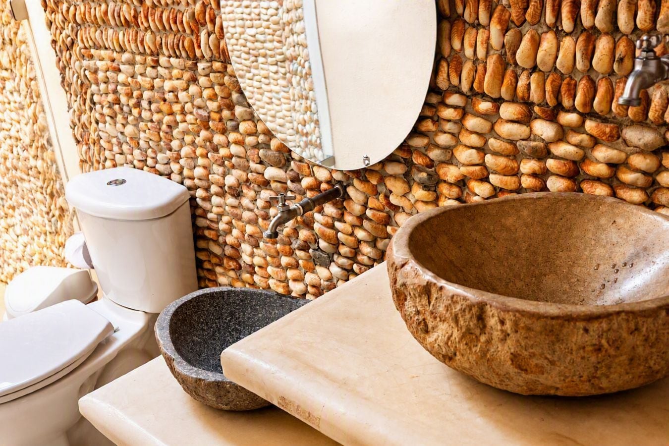 Un baño con pared de piedra, un lavabo con recipiente de piedra y un inodoro.