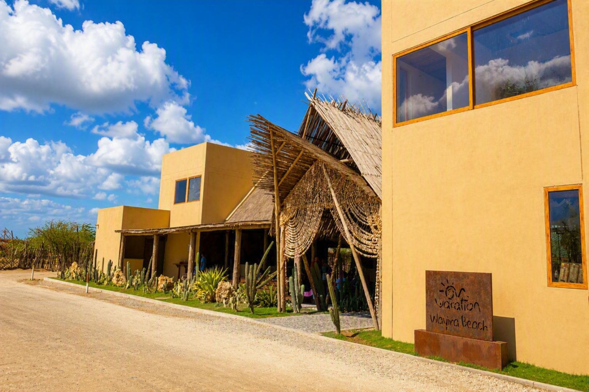 Un complex turístic amb una estructura de teules, un cartell que indica 'Vacation Wayna Beach' i un cel serè.