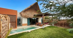 Una casa con techo de paja, piscina y hamaca.