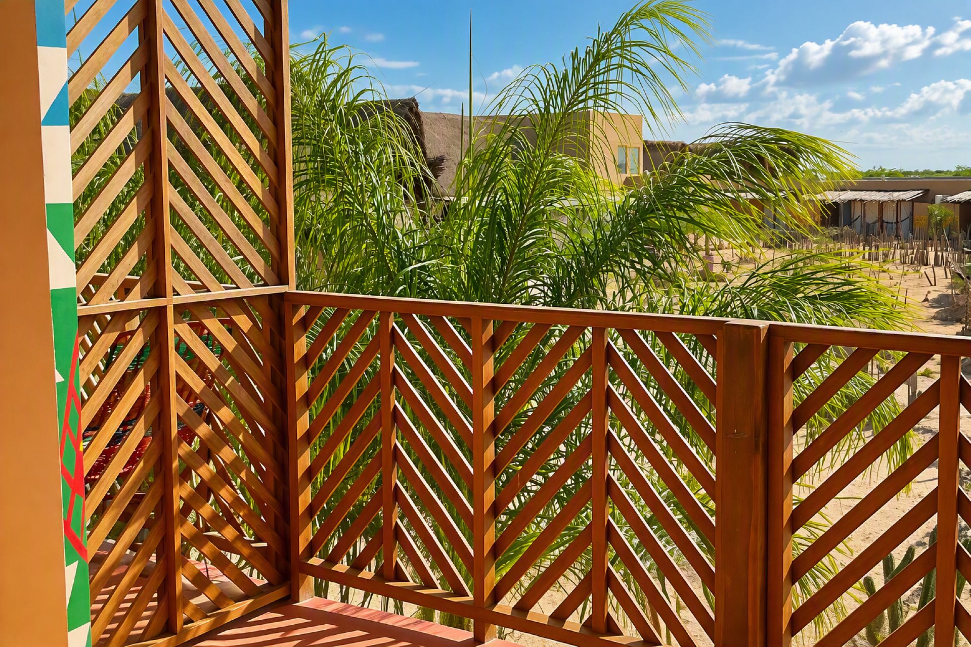 Un balcón de madera con vistas a una zona arenosa y palmeras.
