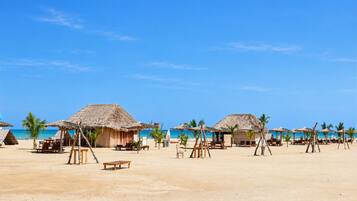 A beach with thatched-roof huts and palm trees.