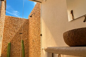 A modern bathroom with a pebble wall, a large stone basin, and a cactus. - Hotel Wayira Beach by On vacation (Manaure)