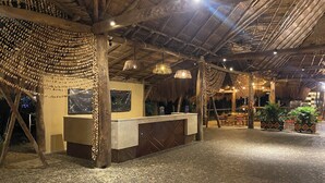 A reception area with a wooden reception desk, hanging decorations, and a thatched roof. - Hotel Wayira Beach by On vacation (Manaure)