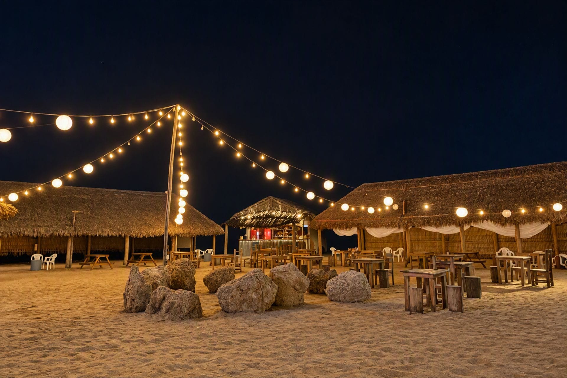 Un complexe hôtelier en bord de mer, doté de bungalows aux toits de chaume, de guirlandes lumineuses et de coins salons en plein air.