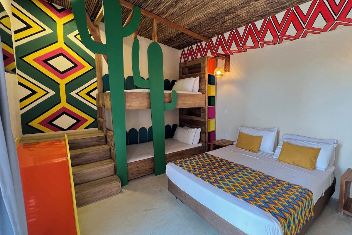 A room with a bunk bed, a colorful geometric wall pattern, a wooden ceiling, and a small bedside table.