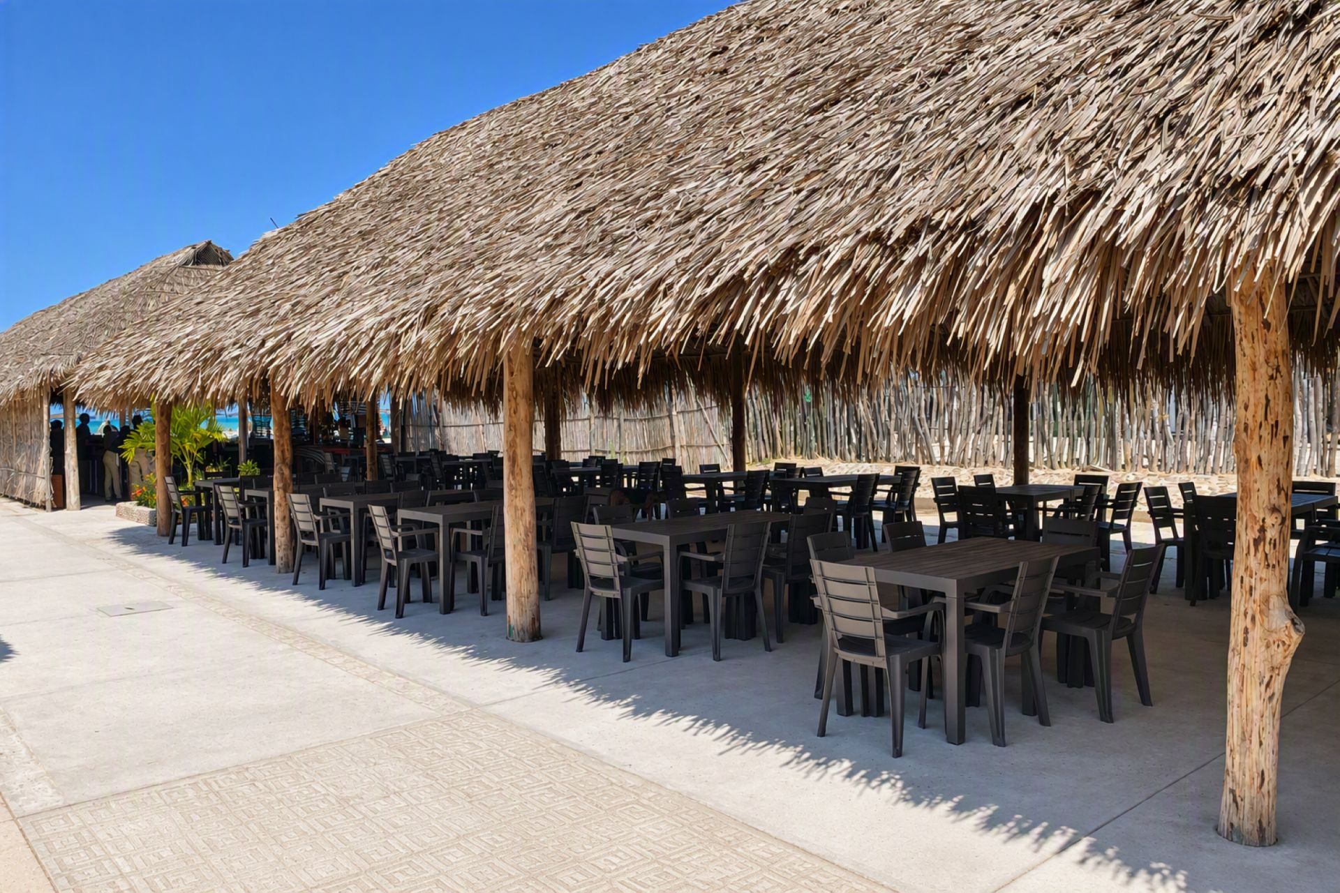 A beachside restaurant with thatched roofs and outdoor seating.