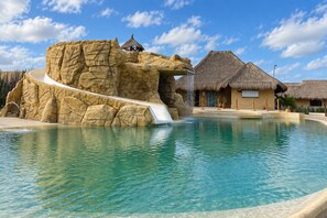 A pool with a rock formation and a waterfall feature. - Hotel Wayira Beach by On vacation (Manaure)