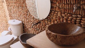 Un baño con lavabo de piedra, recipiente, mortero y pilón, inodoro y espejo.