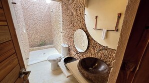 Un baño con pared de piedra, inodoro, lavamanos y ducha.