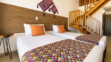 A hotel room with two beds, a wooden headboard, a staircase, and a colorful geometric-patterned bedspread.