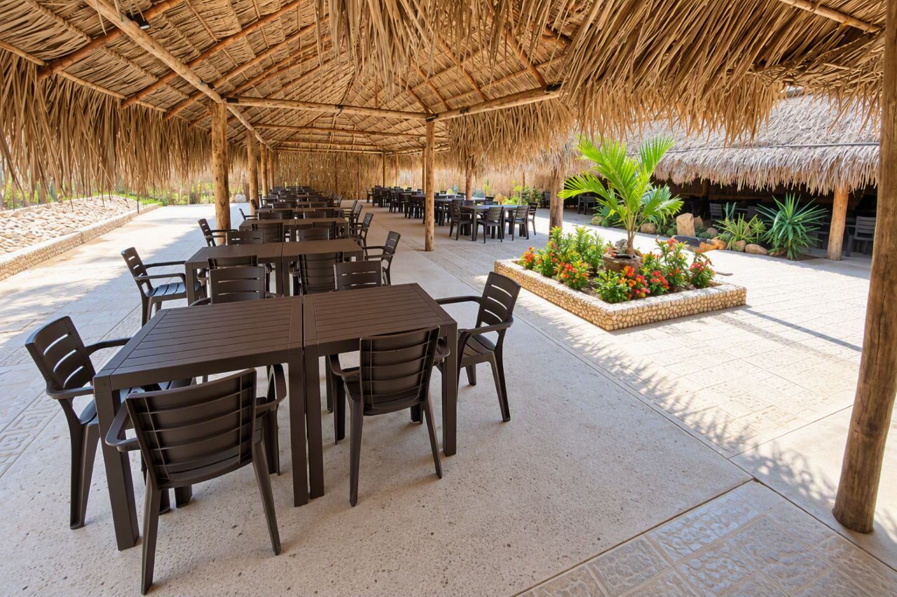 An outdoor dining area with thatched roof, multiple tables, and chairs.