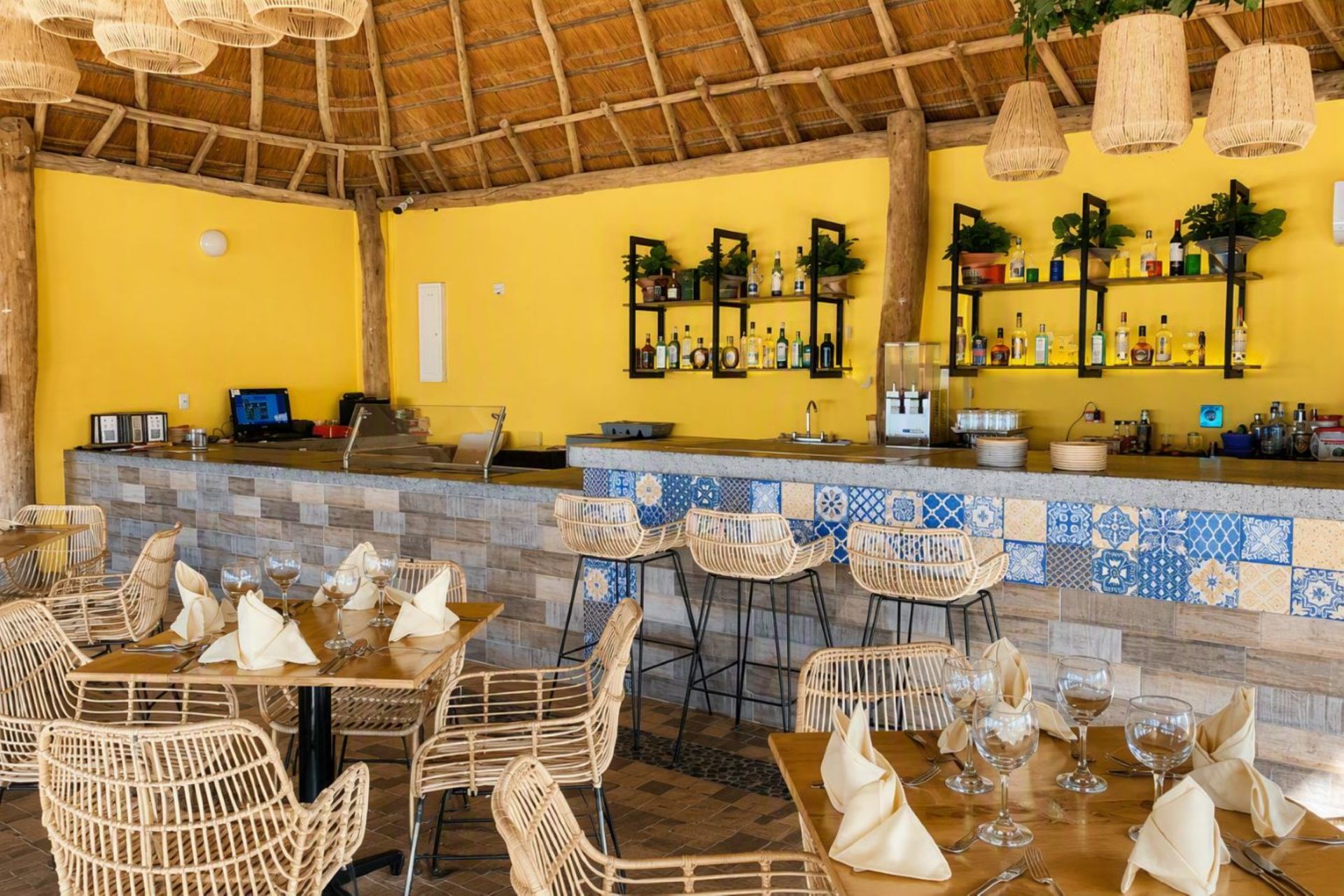 Zona de bar amb un taulell de rajola, cadires de vimet i una paret groga.