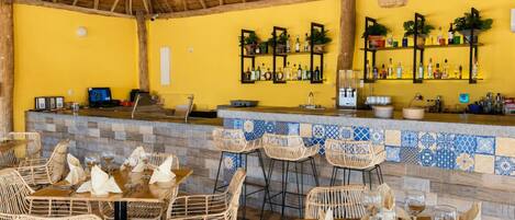 A bar area with a tiled counter, wicker chairs, and a yellow wall.