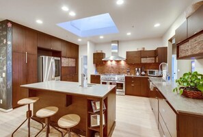 A modern kitchen with a central island, bar stools, a skylight, and built-in appliances.