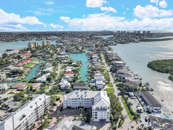 An aerial view of a coastal residential area with a marina, houses, and a large hotel with multiple floors and balconies.