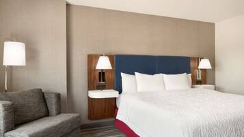 Una habitación de hotel con una cama grande, un sofá, dos mesitas de noche con lámparas y un cabecero de madera.