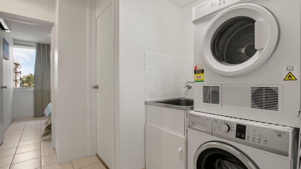 A compact laundry room with a front-loading washer and dryer, a small sink, and a door leading to an outdoor area.