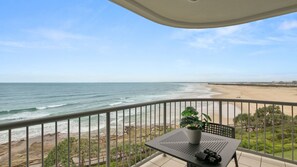 A balcony with a view of the beach and ocean, a potted plant, and a camera on the table.