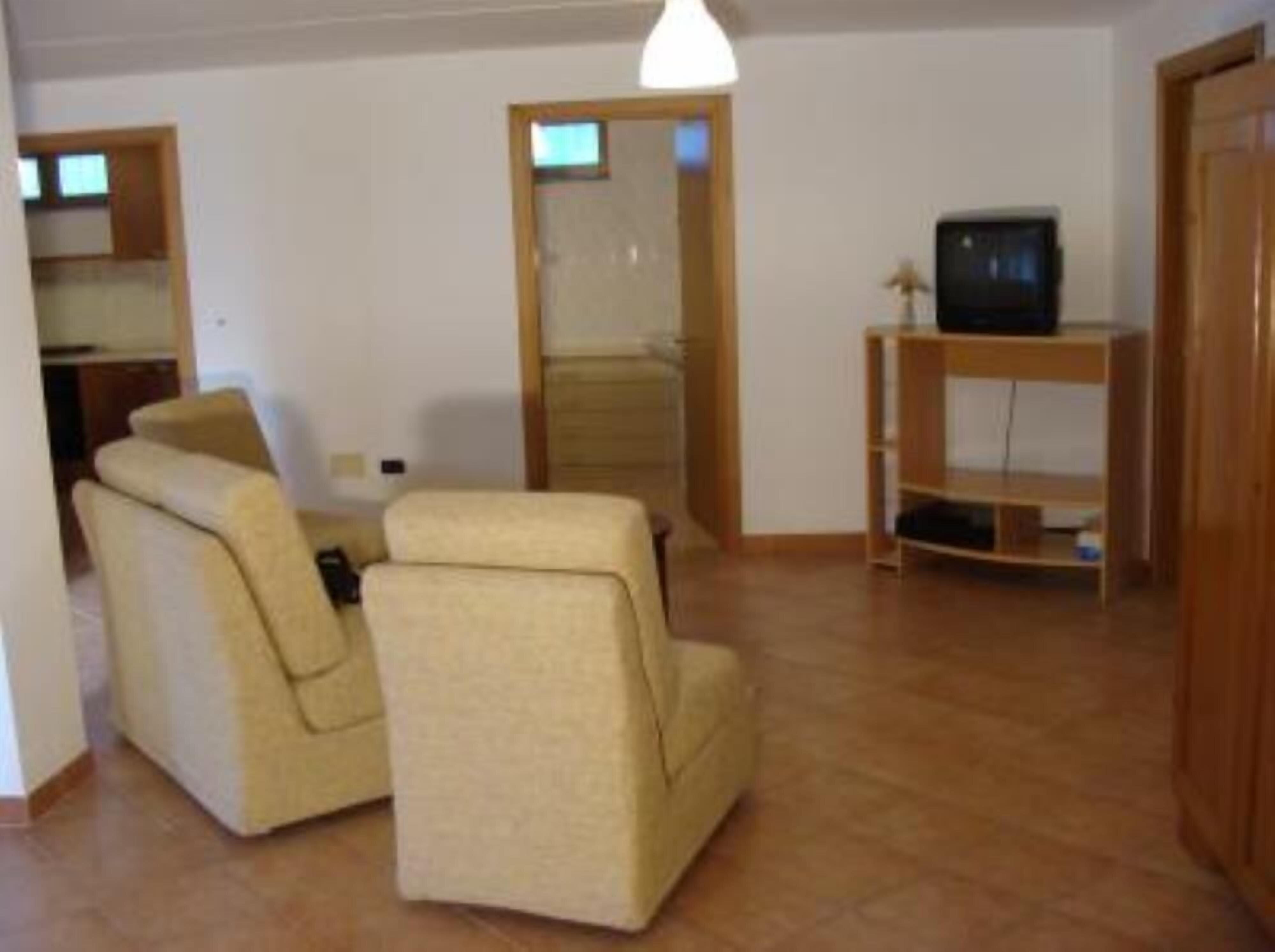Un salón con dos sillones color beige, un mueble de televisión de madera y una puerta que da a otra habitación.