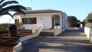 Una casa de dos pisos con techo de tejas, un porche delantero y un camino de entrada pavimentado.