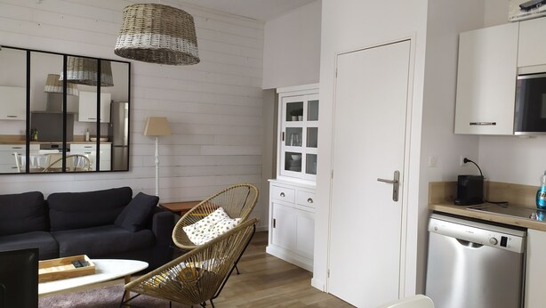 Ein modernes Wohnzimmer mit einem dunkelgrauen Sofa, einem Korbstuhl, einem kleinen Tisch und einem großen Spiegel an der Wand.