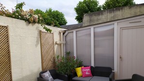 Eine Terrassenfläche mit Korbmöbeln, einem grünen Teppich und einer Wand mit Kletterpflanzen.