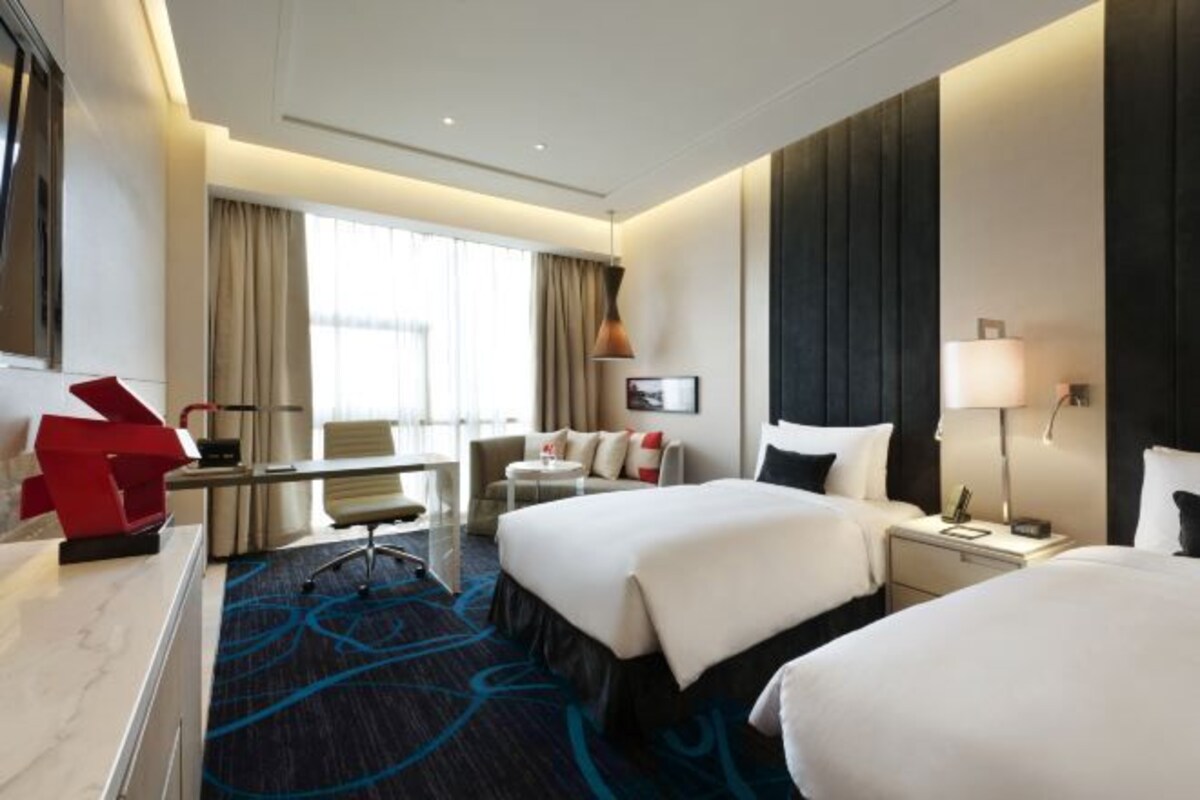 A hotel room with two beds, a desk, a chair, a lamp, and a window with curtains.