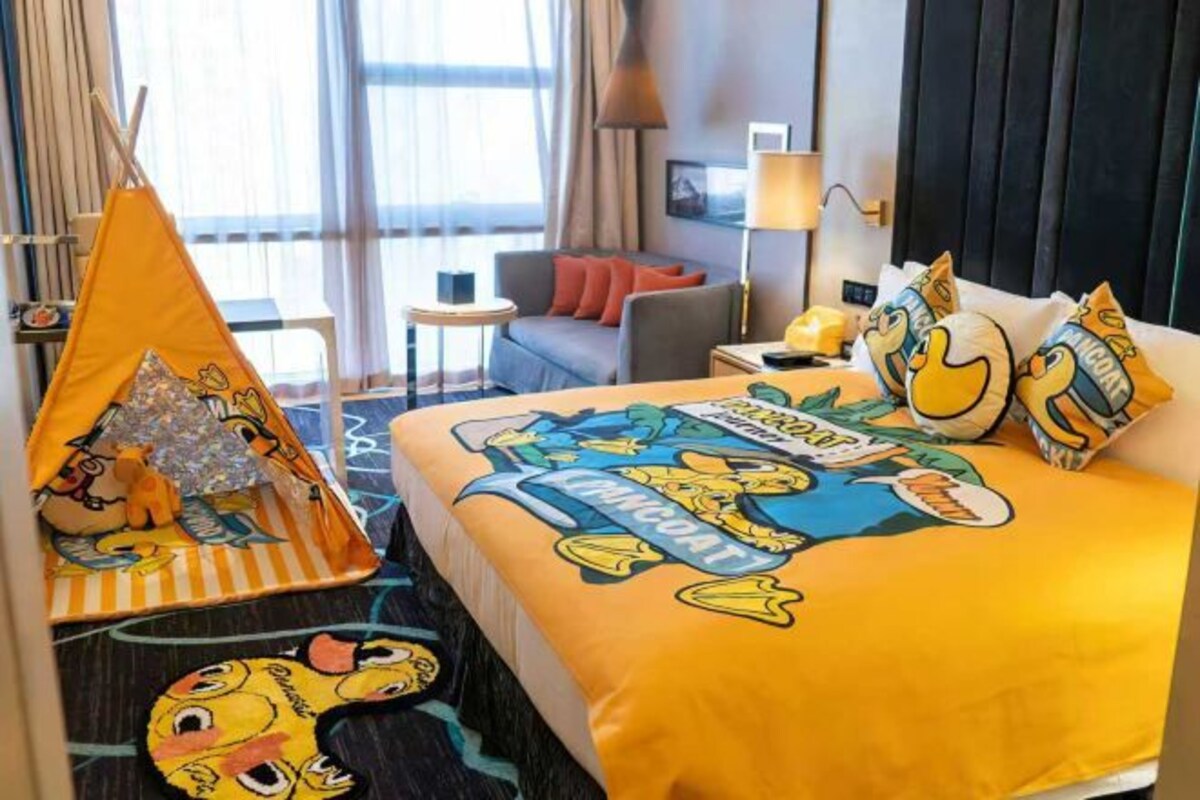 A hotel room with a bed featuring a cartoon character design, a small play tent, and a view of the outdoors.