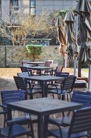 An outdoor patio with tables and chairs, a stone wall, and a small tree. - Hilton Xi'an High-tech Zone (Xi'an)