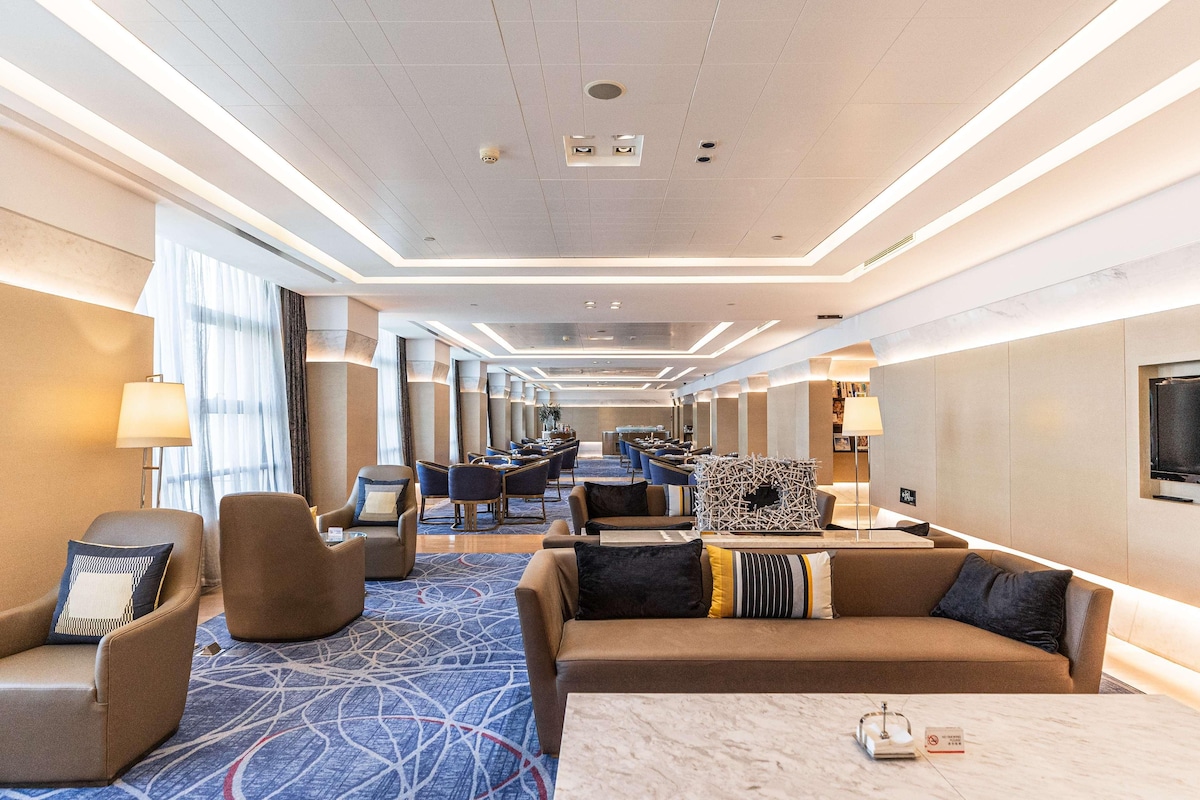 A hotel lobby with seating areas, a reception desk, and a large TV screen.